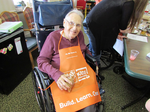 An elderly individual enjoying a community crafting activity while seated in a wheelchair, wearing an orange apron.