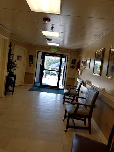 A well-lit hallway featuring a waiting area with chairs and a clear entrance door.