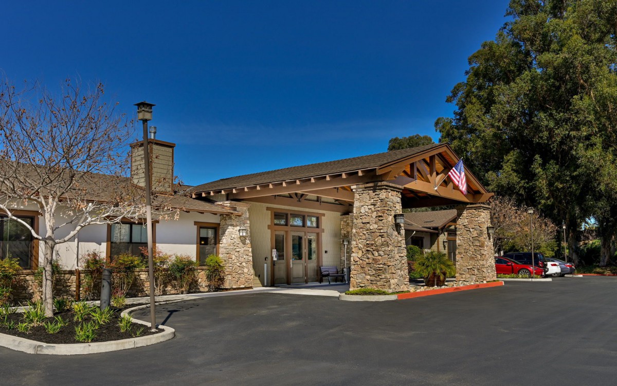 A building entrance with a stone facade and an American flag under a clear blue sky.