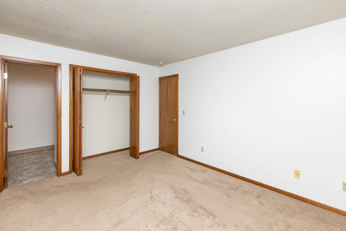An empty room with carpet flooring, a wooden closet, and a door against white walls.