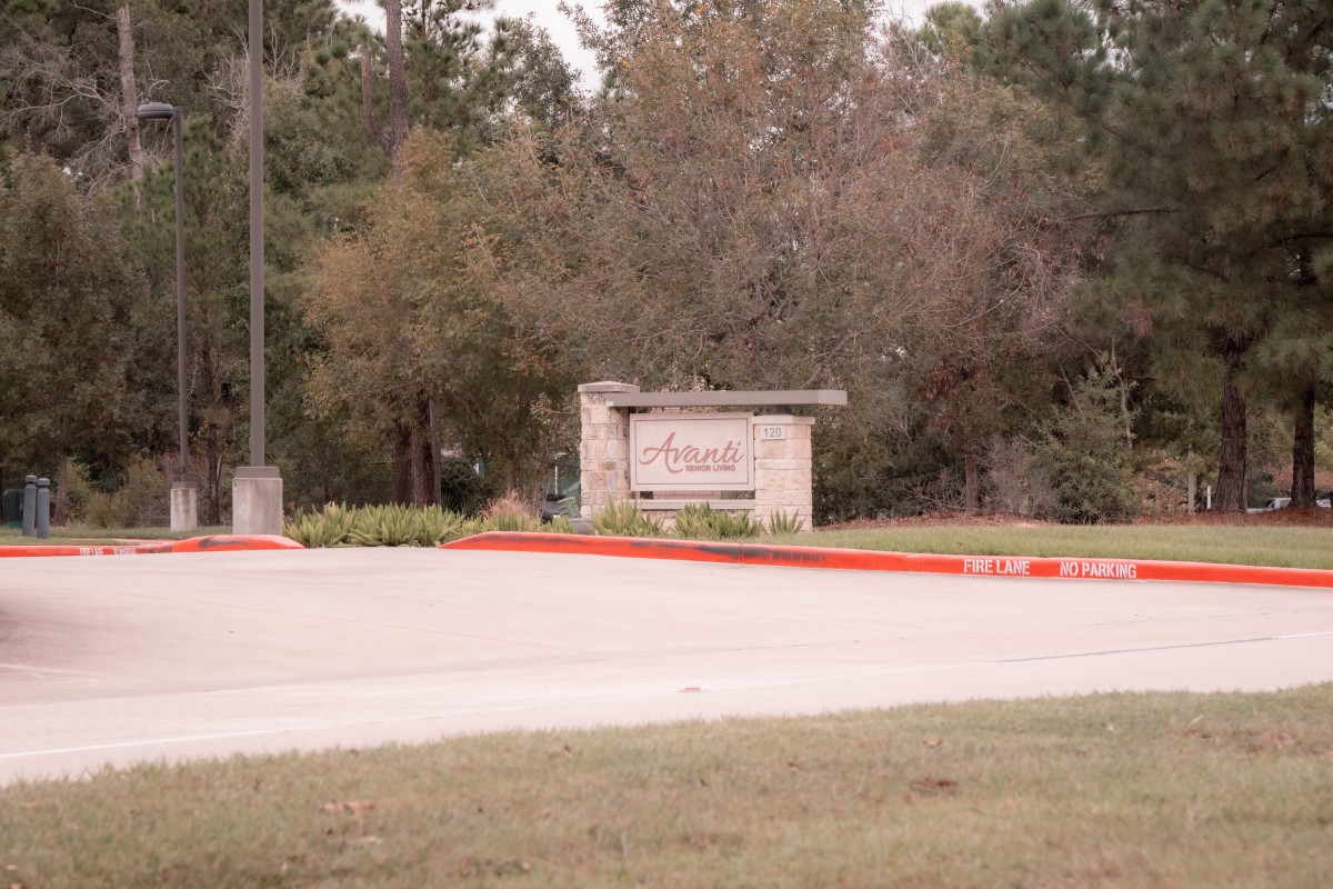 Entrance sign surrounded by trees and a road.