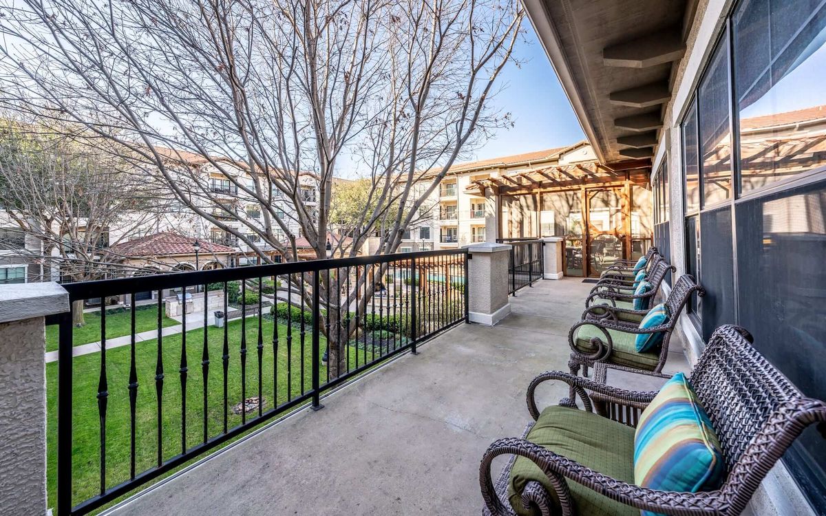 A spacious balcony with comfortable chairs overlooks a peaceful courtyard in an apartment complex.