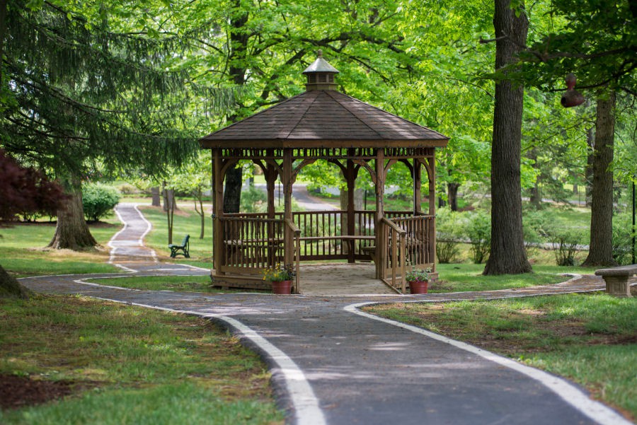 A wooden gazebo situated in a lush green park, surrounded by trees and accompanied by a winding pathway.