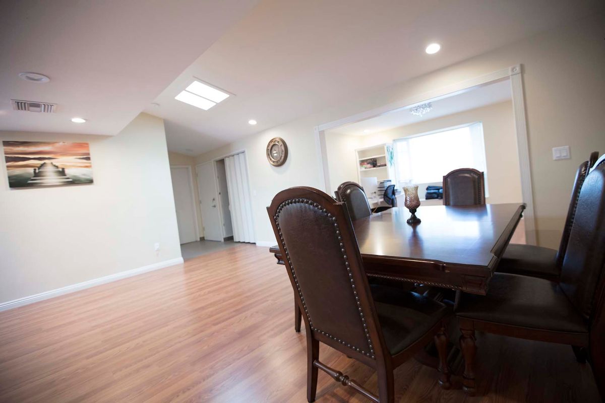 A spacious dining room with a large wooden table and chairs, featuring bright lighting and a wooden floor.