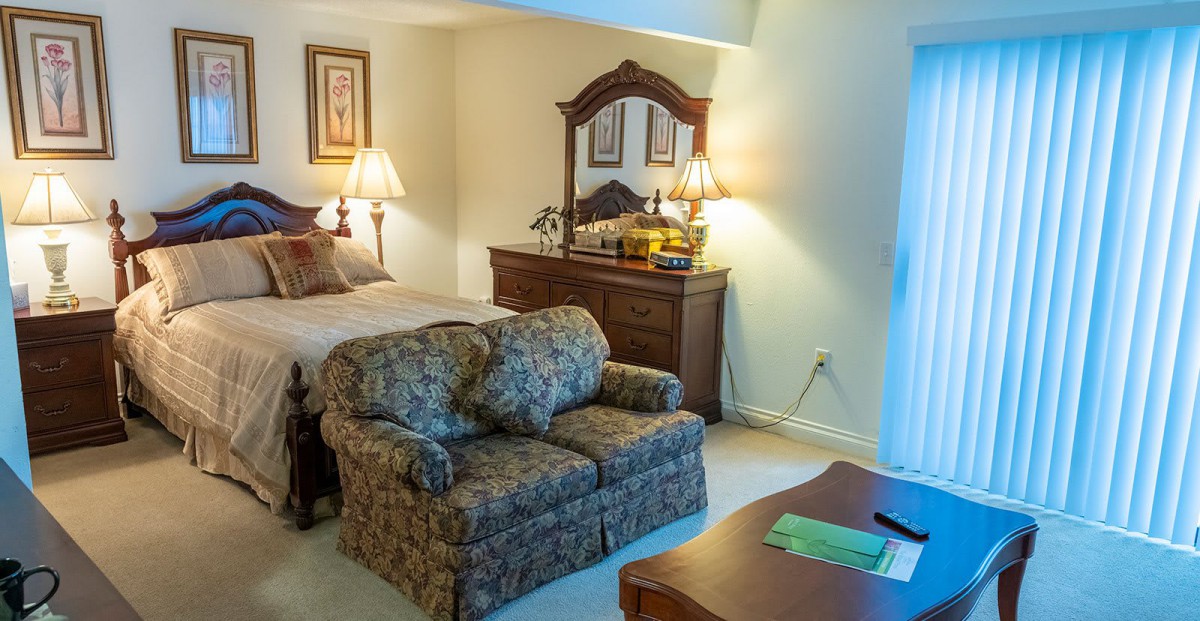 A cozy bedroom featuring a bed, a patterned sofa, and elegant wooden furniture with warm lighting.