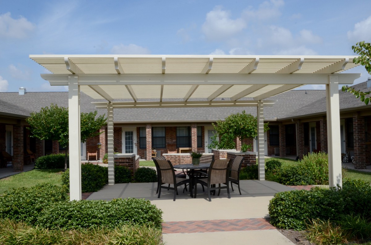 A patio with a pergola providing shade over an outdoor dining set, surrounded by well-maintained garden landscaping.