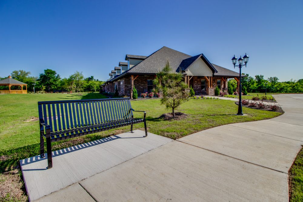 A sunny day at a park featuring a building, bench, and lush greenery.