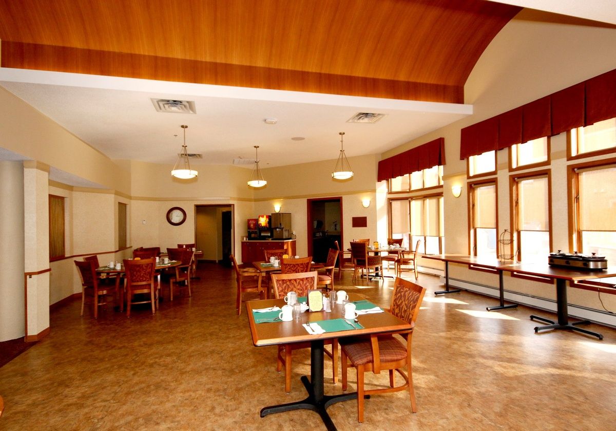 A cozy dining area with wooden tables and chairs, set in a room with large windows and warm lighting.