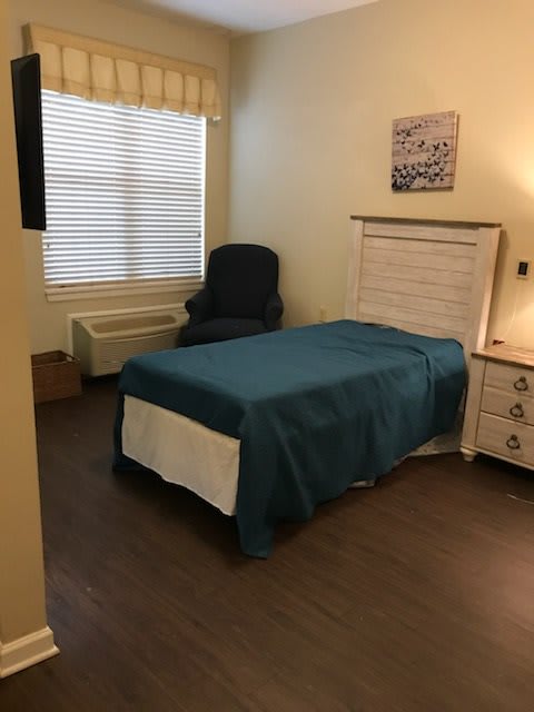 A simple bedroom with a single bed, chair, and window.