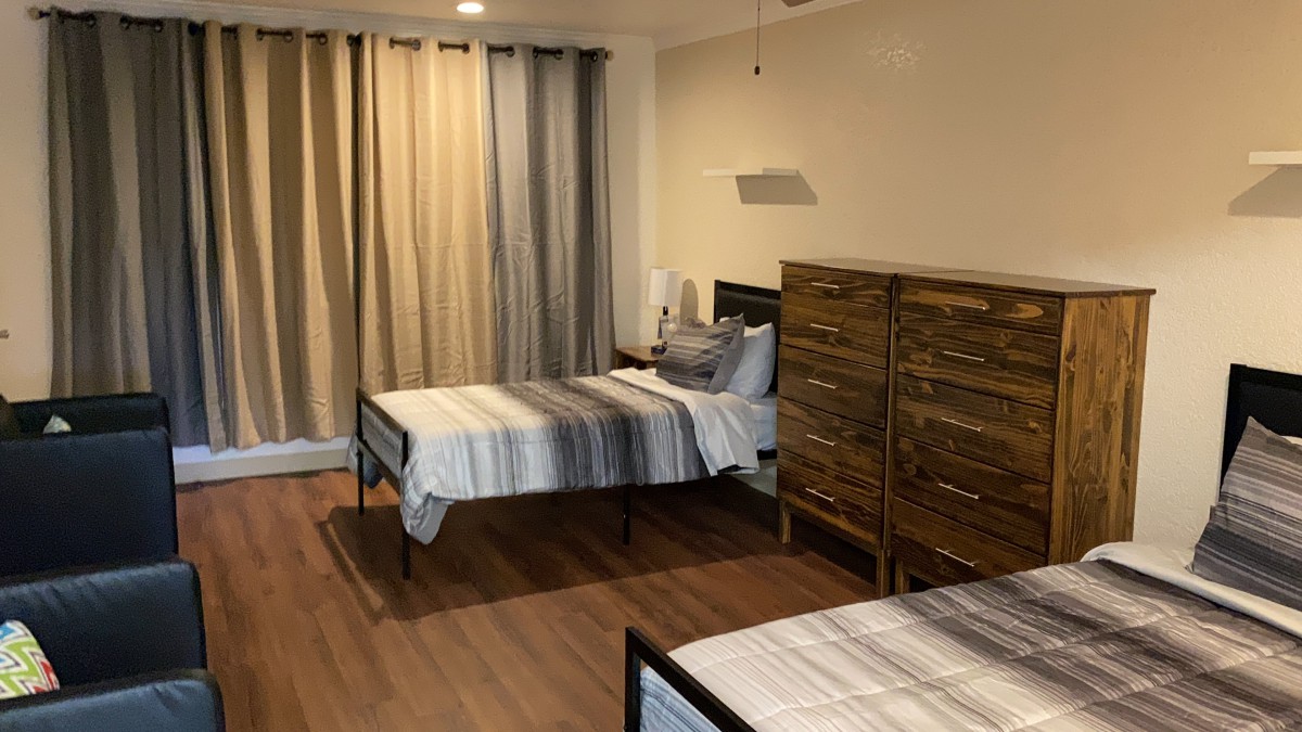 A cozy bedroom with two twin beds, a wooden dresser, and soft drapes filtering the light.