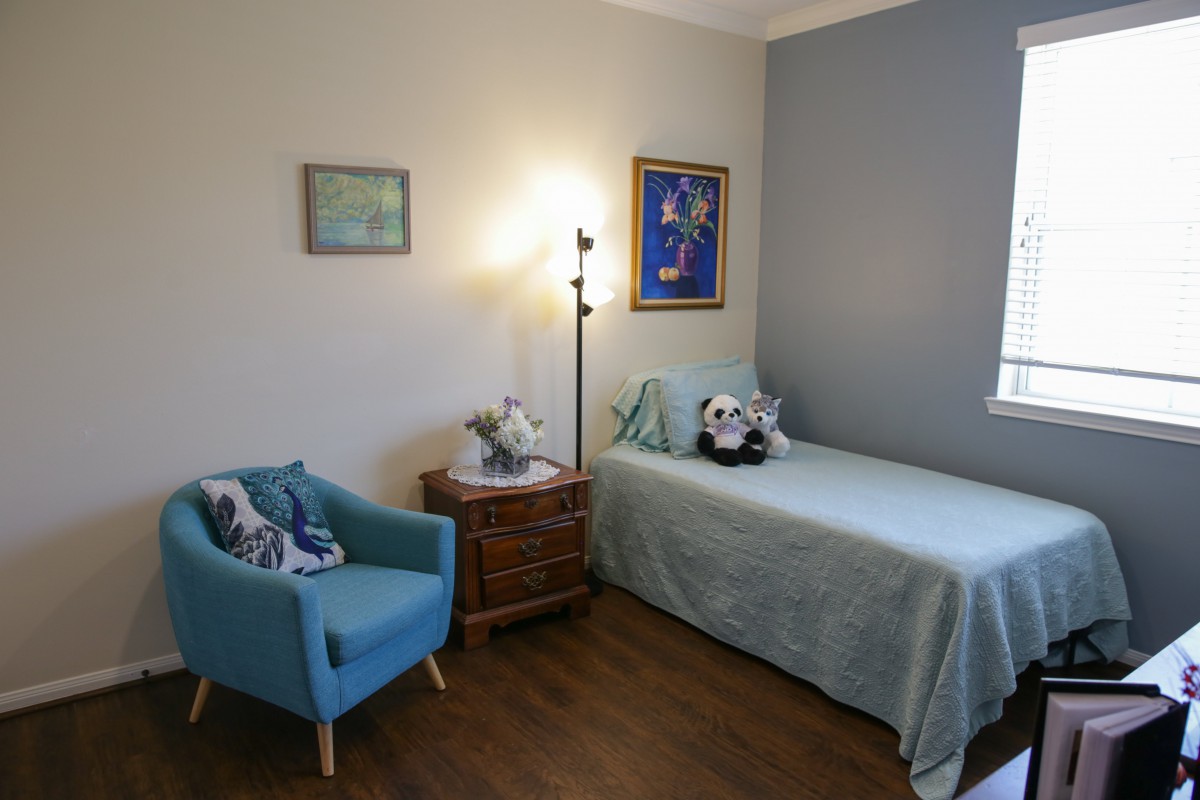 A cozy bedroom featuring a single bed with decorative pillows, a blue armchair, and framed artwork on the walls.