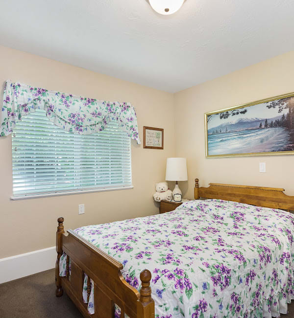 A cozy bedroom featuring a floral bedspread, wooden bed frame, and wall art with a window view.