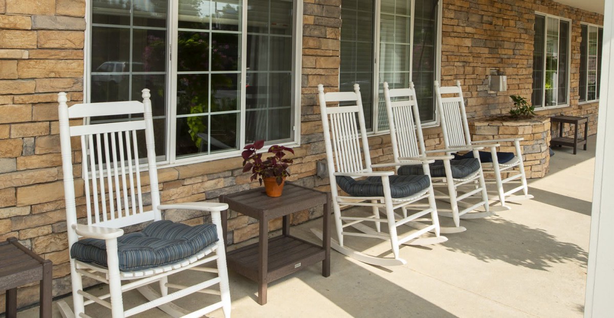 A row of rocking chairs on a porch with a small table and potted plant.