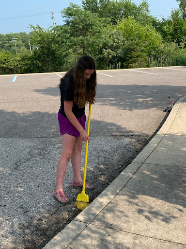 A young woman uses a yellow tool to clean the curb on a sunny day.