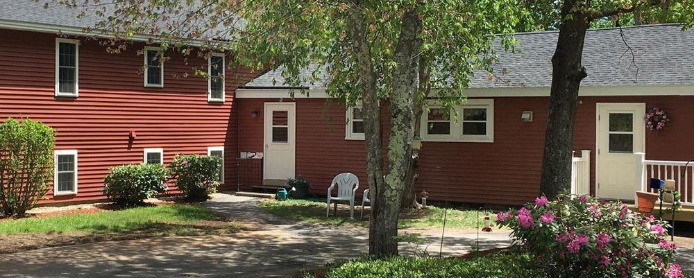 A red house with a backyard featuring trees and plastic chairs.