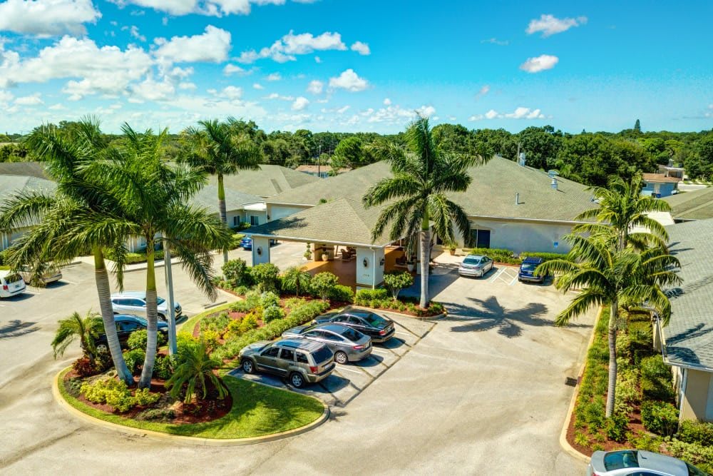 Aerial view of a parking lot surrounded by palm trees and buildings under a bright blue sky.