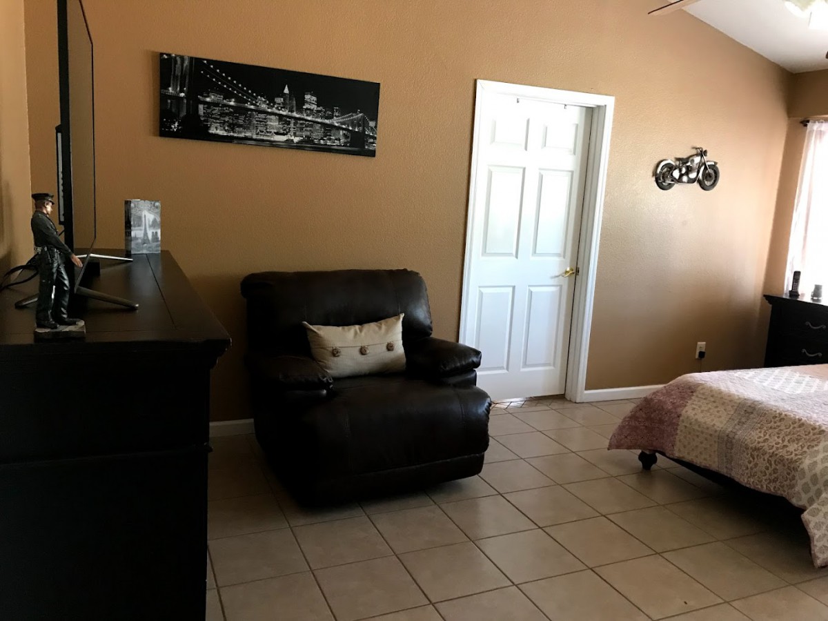 A cozy living room featuring a black armchair with a decorative pillow, complemented by wall art and tile flooring.