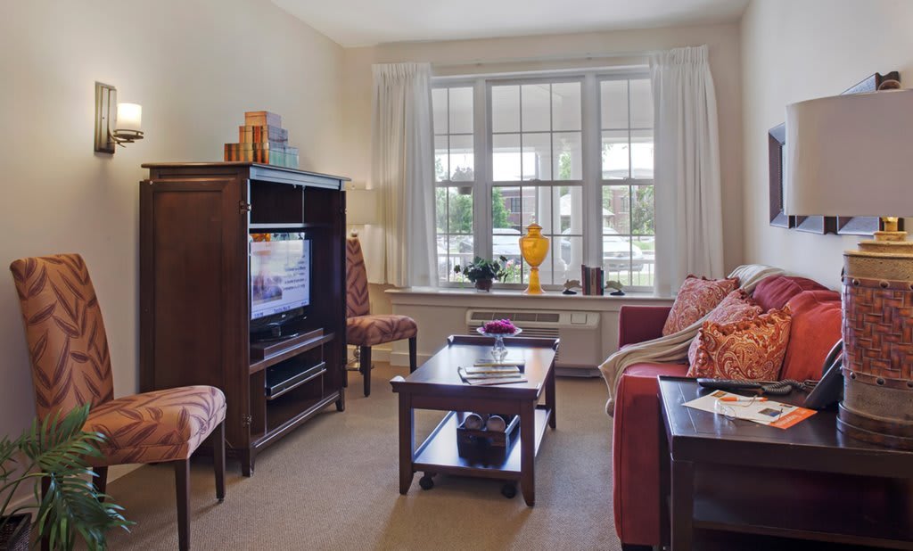 A cozy living room with a sofa, coffee table, and television, featuring large windows and tasteful decor.