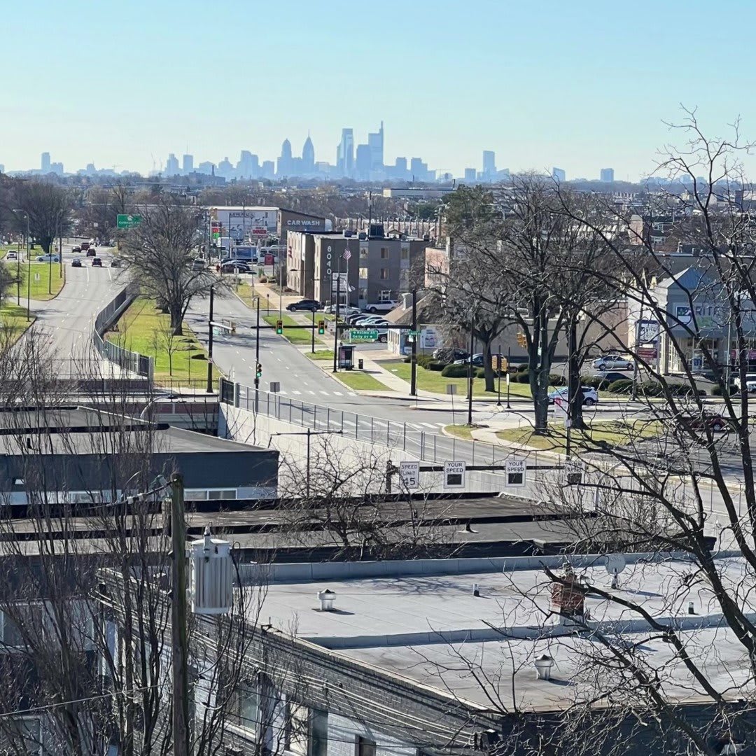 A view of a city skyline from a suburban neighborhood with roads, buildings, and trees.
