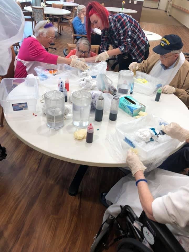 A group of people engaged in a tie-dye craft activity at a round table, using various colored dyes.