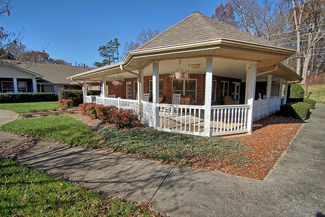 A charming house with a wraparound porch and well-maintained garden on a sunny day.