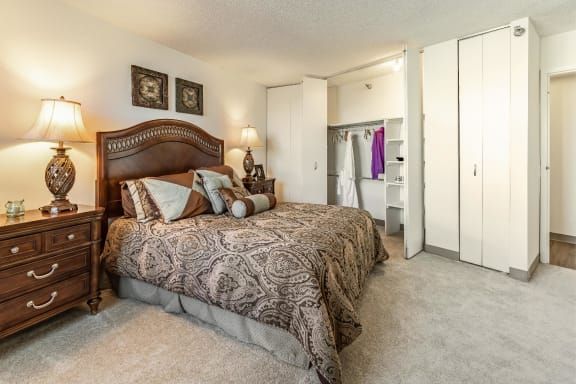 A cozy bedroom with a patterned bedspread, decorative pillows, and an open closet.