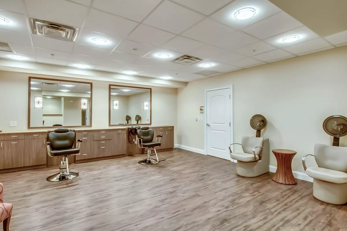 An empty salon with barber chairs, mirrors, and a hair dryer on a wooden floor.