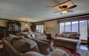 A cozy and well-decorated living room with plush seating, ceiling fan, and large windows.