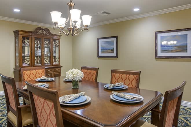 A neatly arranged dining room with a wooden table set for four, under a decorative chandelier.
