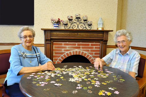 Two elderly women enjoying a puzzle together in a cozy indoor setting.