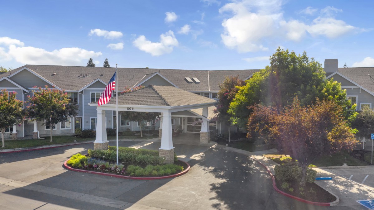 A building entrance with American flags, surrounded by trees and a clear sky.