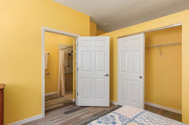 A bright bedroom with yellow walls, featuring open doors leading to a closet and adjacent room.