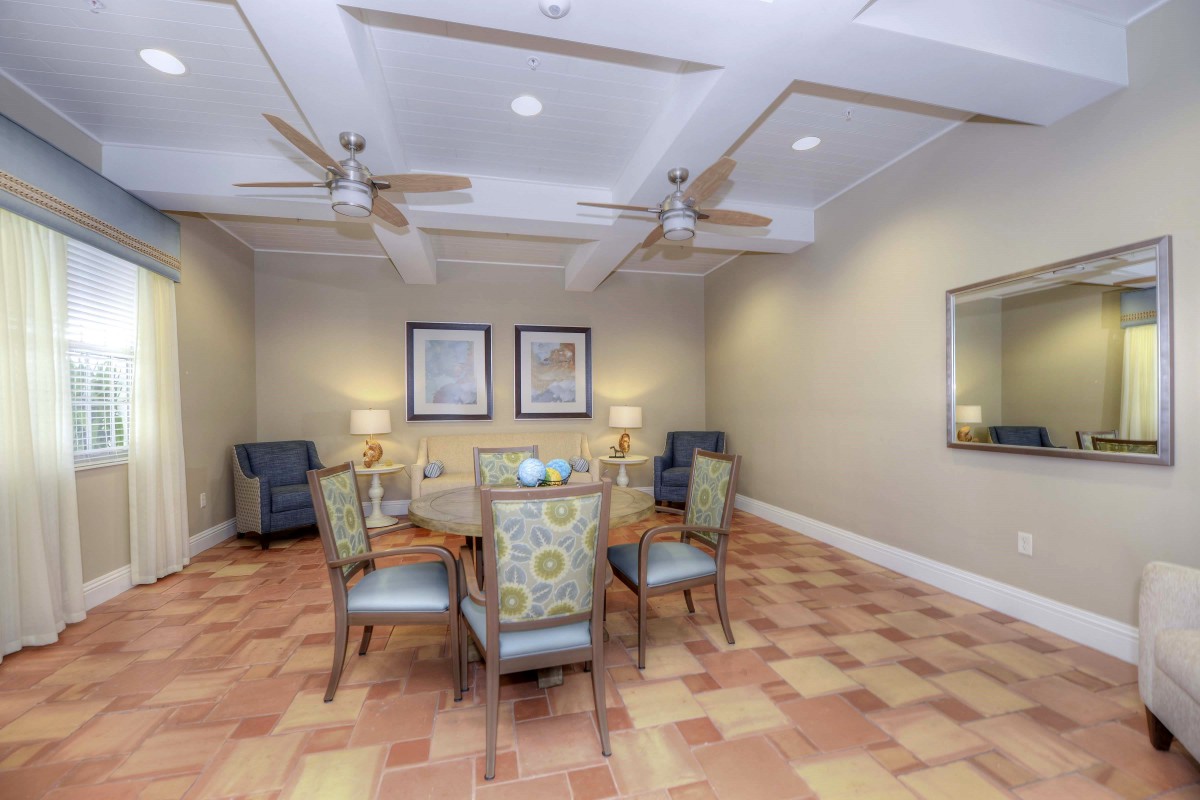 A cozy dining room with a glass table and upholstered chairs, complemented by ceiling fans and framed artwork on the walls.