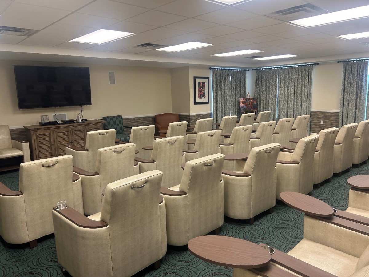 A spacious conference room with multiple rows of comfortable chairs facing a television.