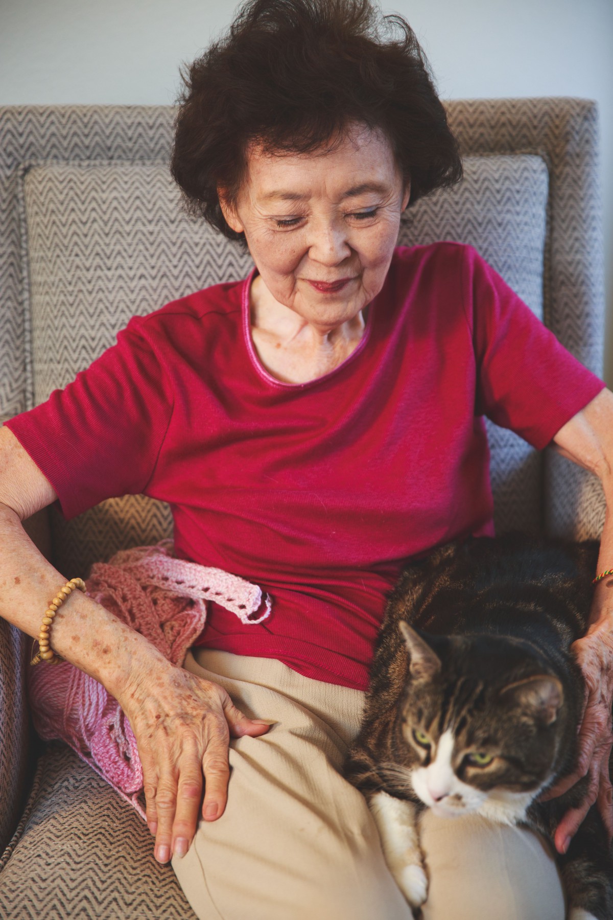 A smiling elderly woman sitting indoors with a cat on her lap.