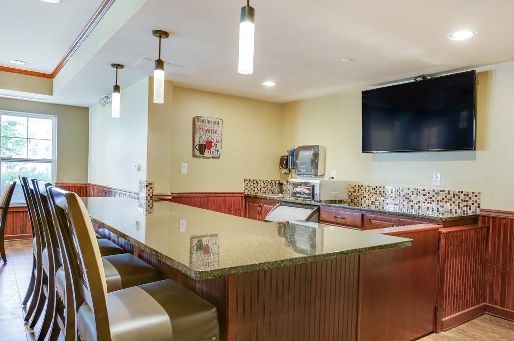 A modern kitchen area featuring a sleek countertop with bar stools, overhead lighting, and a wall-mounted television.