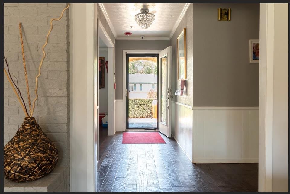 A bright hallway with a door leading outside, featuring a red mat and overhead light fixture.