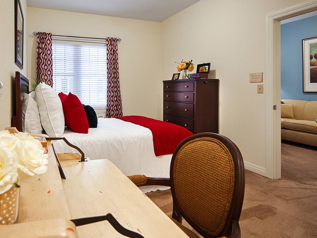 A cozy bedroom with a bed adorned with red and white linens, wooden dresser, and decorative curtains.