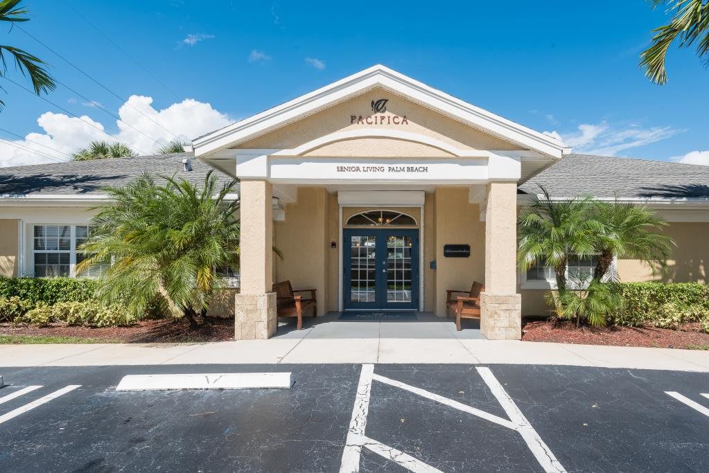 A small building with a welcoming entrance, featuring palm trees and a parking area under a clear blue sky.
