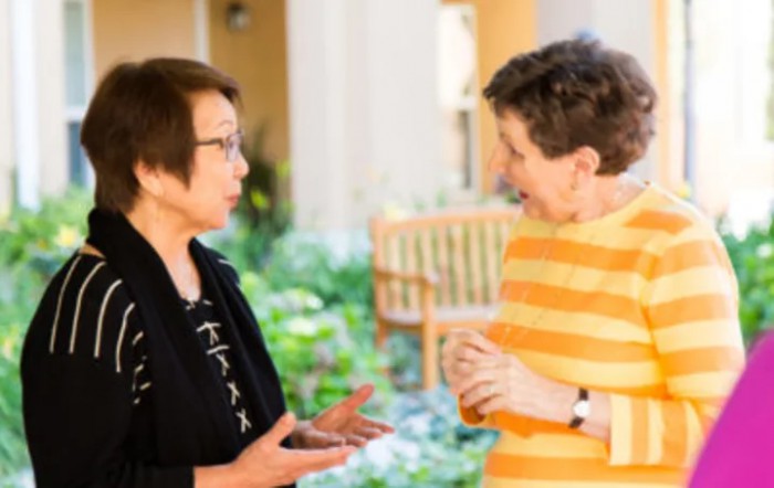 Two individuals engaged in a conversation in a garden setting.