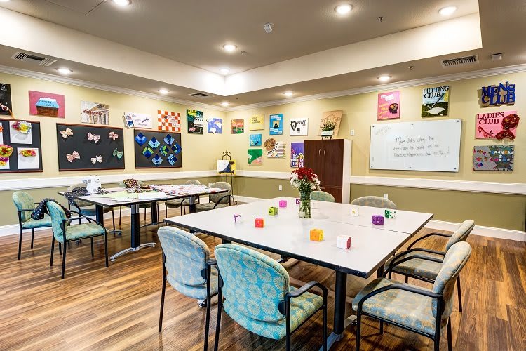 A well-lit classroom featuring artwork on the walls, tables, and chairs arranged for creative activities.