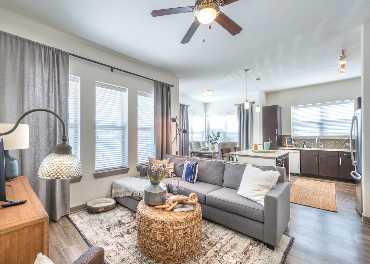 A modern open-concept living room with a comfortable sofa, wicker coffee table, and adjoining kitchen area.