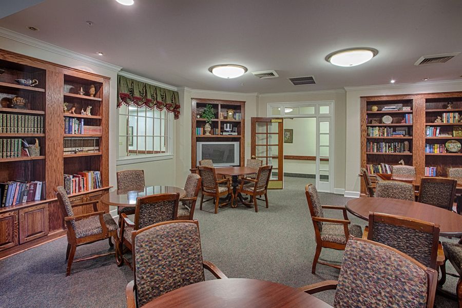 A cozy library room with bookshelves, tables, and chairs designed for reading and study.
