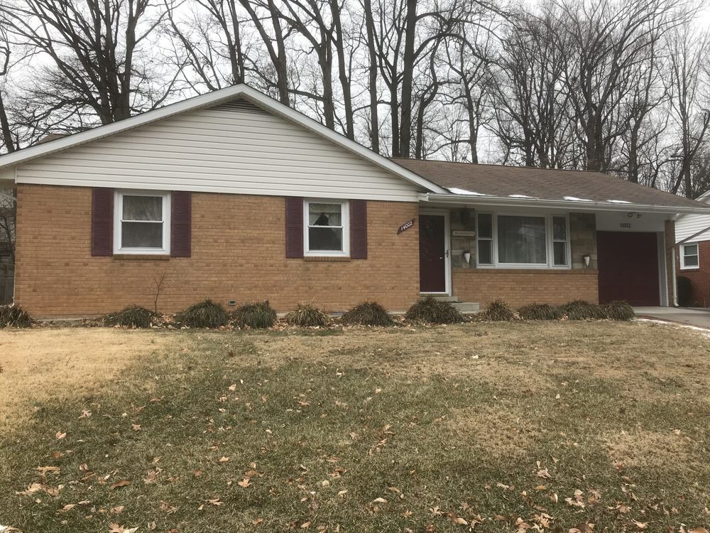A single-story ranch-style brick house with a front yard and surrounding trees.