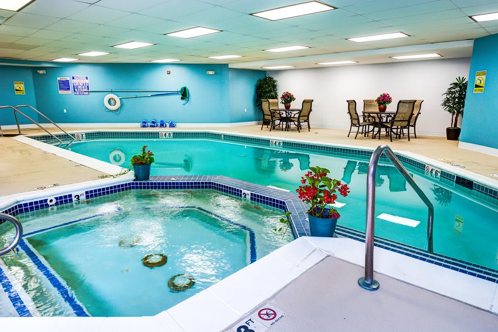 An inviting indoor swimming pool with a jacuzzi, surrounded by seating and plants for relaxation.