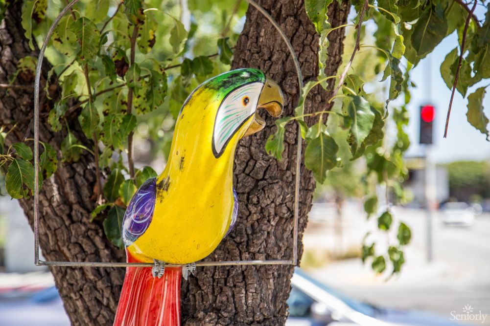 A colorful parrot sculpture hanging on a tree outdoors.
