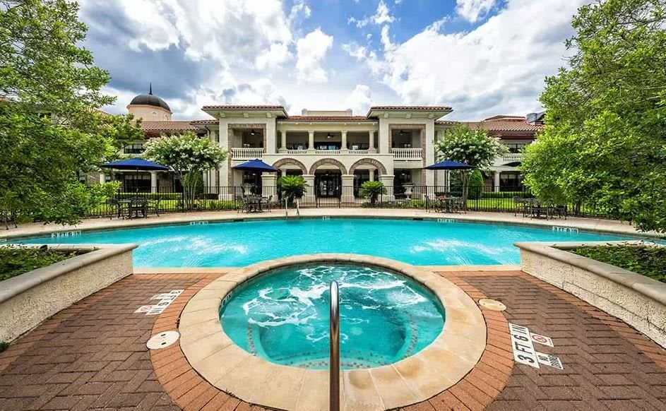 A luxurious outdoor pool and hot tub in front of a grand building, perfect for a relaxing vacation.