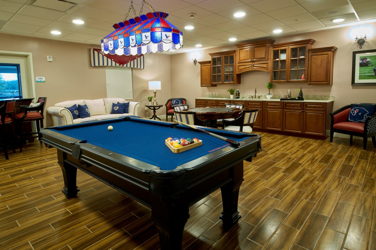A cozy game room featuring a blue pool table, comfortable seating, and a bar area.