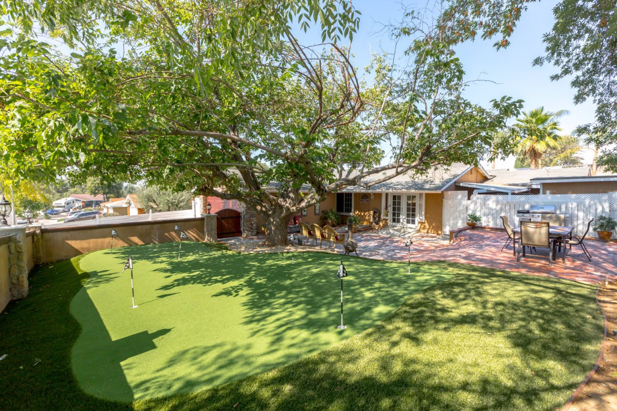 A serene backyard with a large tree and well-maintained lawn, adjacent to a cozy house with a patio.