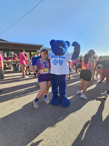 A participant poses happily with a blue bear mascot at a lively outdoor event.